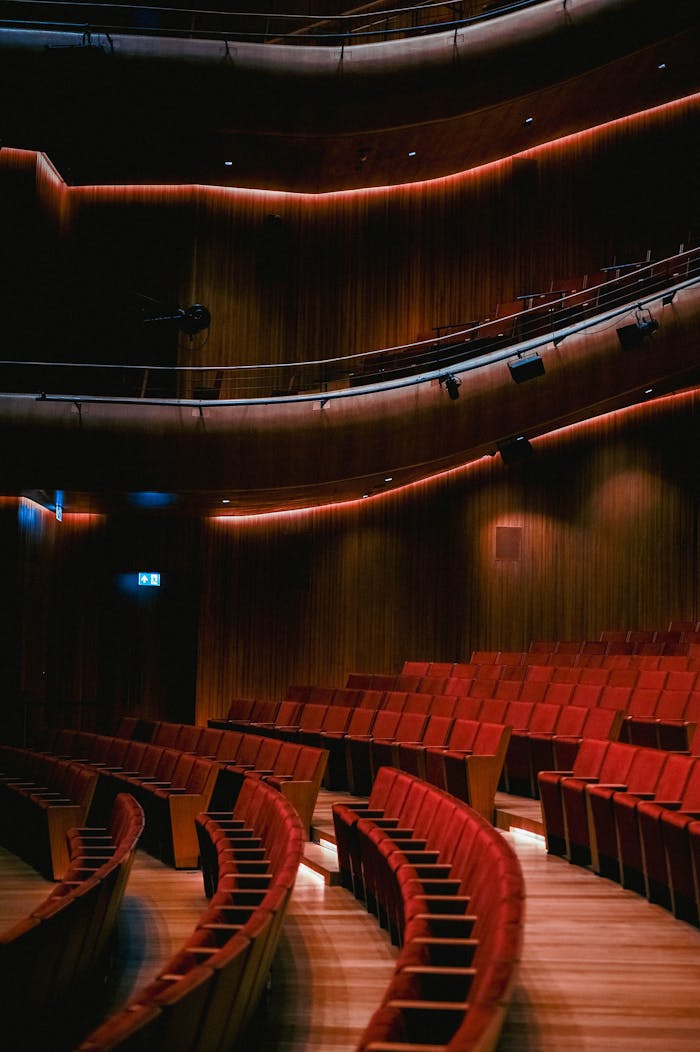 A beautifully lit theater with curved rows of red seats and wood paneling.